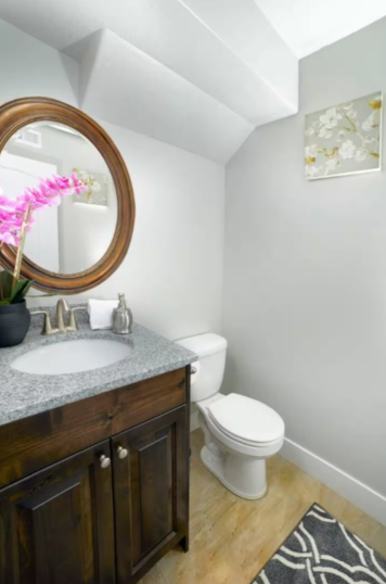 Second bathroom with dark wood vanity, granite countertop, round mirror and pink orchid