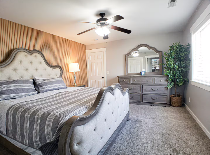 Master bedroom with tufted king bed, striped wood accent wall and dresser with mirror