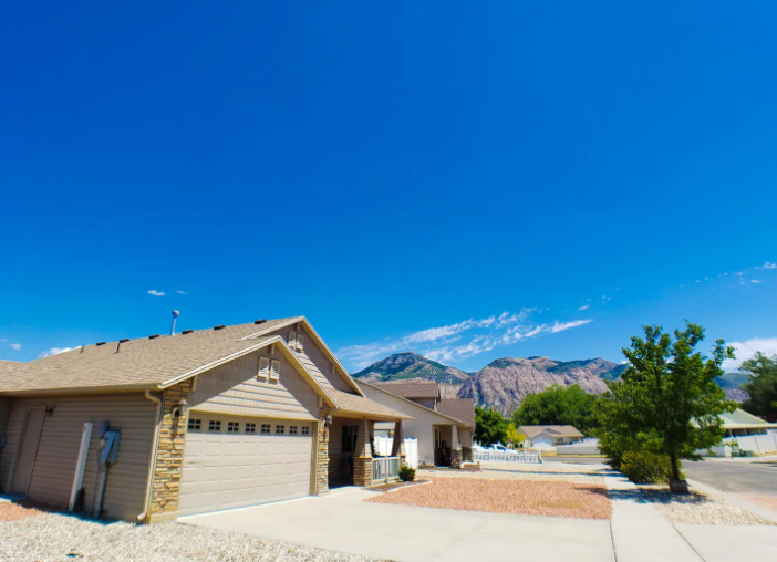 Single-level home exterior with 2-car garage, stone accents and dramatic Wasatch Mountain backdrop under blue sky