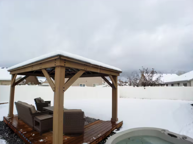 Snow-covered backyard with cedar gazebo, wicker seating and bubbling hot tub