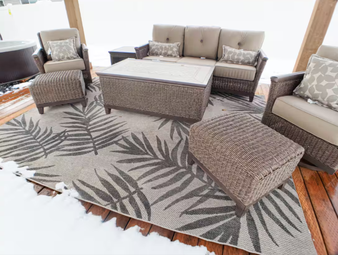 Covered gazebo with wicker sectional seating, fire table and tropical rug on wood deck in winter