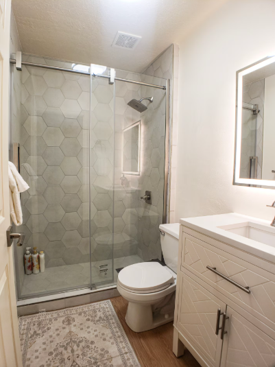 Modern bathroom with hexagon tile walk-in shower, glass slider enclosure, white vanity, LED mirror and wood-look floors