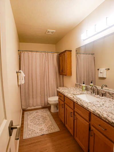 Full bathroom with granite countertop double vanity, oak cabinets, shower-tub combo with curtain and large mirror