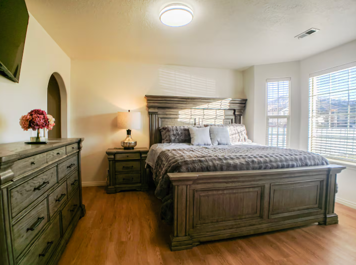 Master bedroom with large dark wood panel bed, matching dresser, warm lamp and mountain views through window