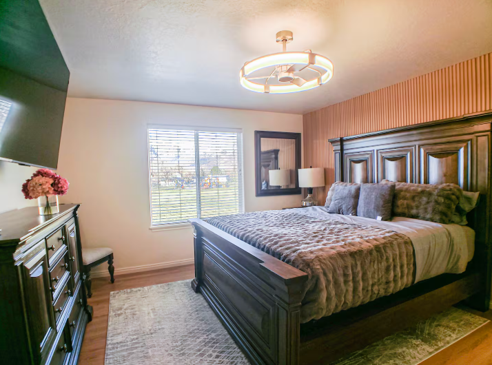 Spacious bedroom with dark wood king bed, striped accent wall, modern ceiling fan light and natural light