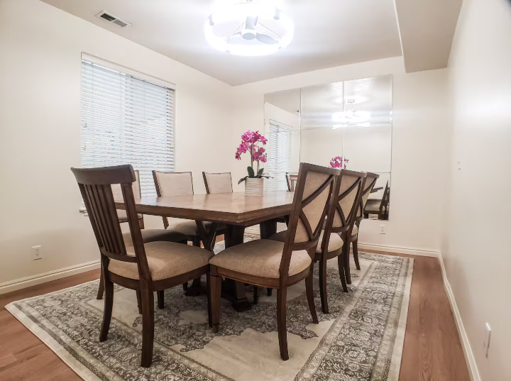 Formal dining room with dark wood table seating 8, upholstered chairs, pink orchids and full-wall mirror