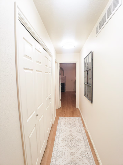 Bright hallway with white panel doors, hardwood floors, decorative rug and framed wall art leading to living area