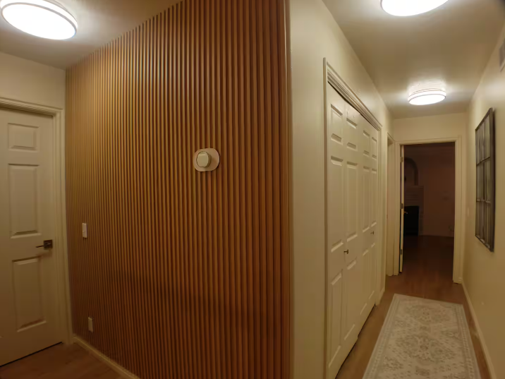 Wide hallway with dramatic vertical wood slat accent wall, flush-mount ceiling lights and decorative runner rug