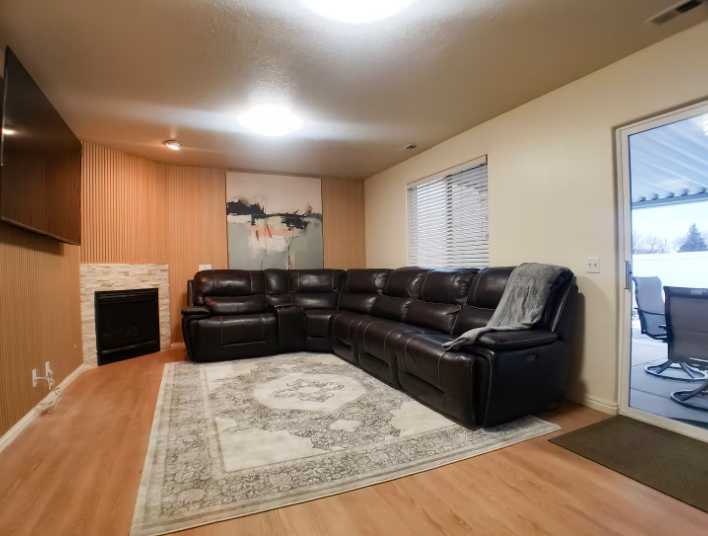 Living room with large dark leather reclining sectional, stone fireplace, wood slat accent wall, large TV and patio door