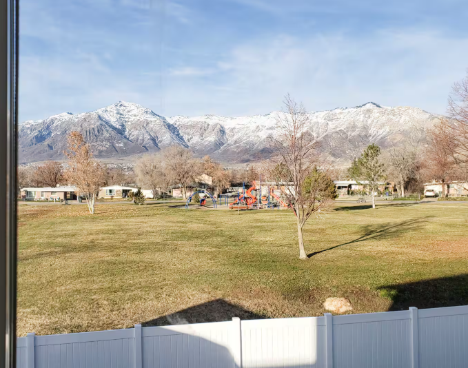 Panoramic view of snow-capped Wasatch Mountains over white vinyl fence with Rose Wagner Park in foreground