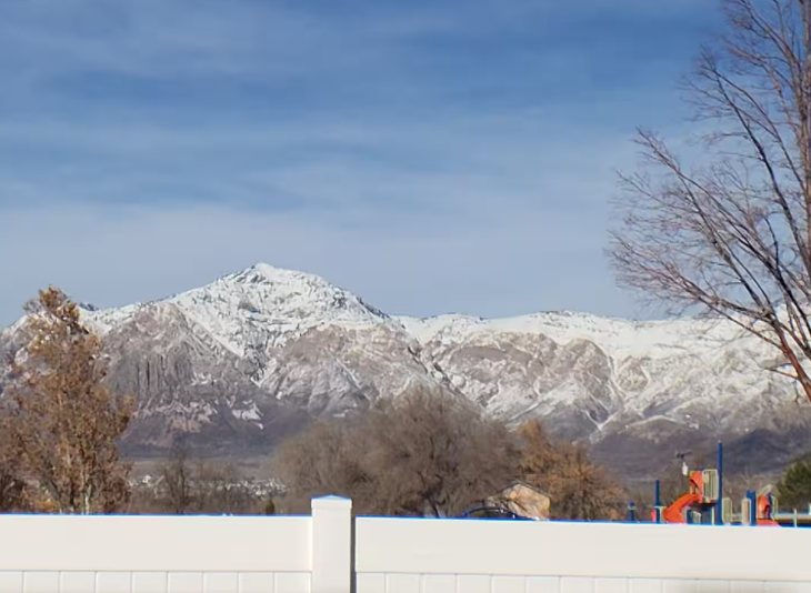 View from backyard over white vinyl fence to Rose Wagner Park playground with snow-capped Wasatch Mountains behind