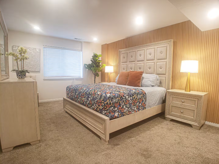 Master bedroom with tall tufted upholstered headboard, wood slat accent wall, floral bedding and warm bedside lamps