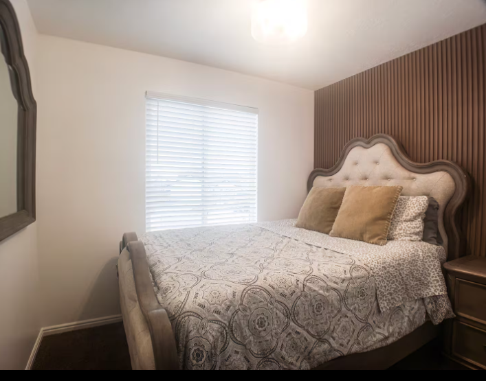 Bedroom with ornate tufted sleigh bed, wood slat accent wall and natural light from window