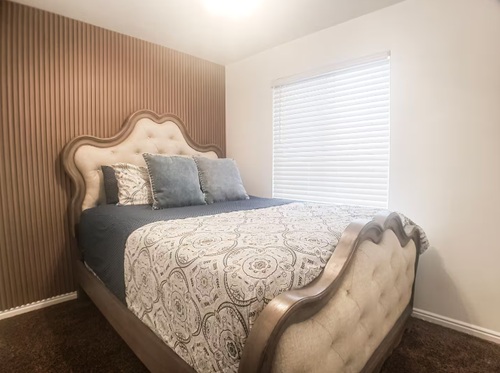 Cozy bedroom with ornate tufted sleigh bed, blue accent pillows, wood slat accent wall and natural light
