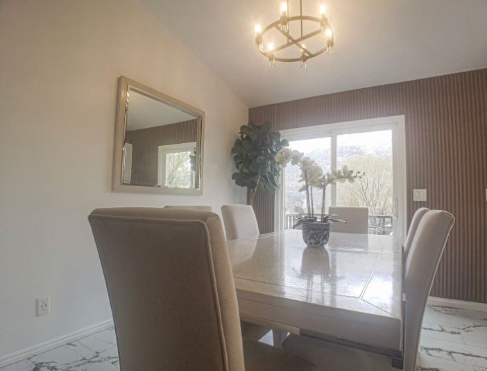 Dining room with vaulted ceiling, modern chandelier, wood slat accent wall, marble tile floors and mountain views through sliding glass door