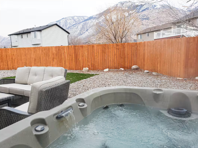 Private hot tub with waterfall jets, patio seating, cedar fence and snow-capped Wasatch Mountain views