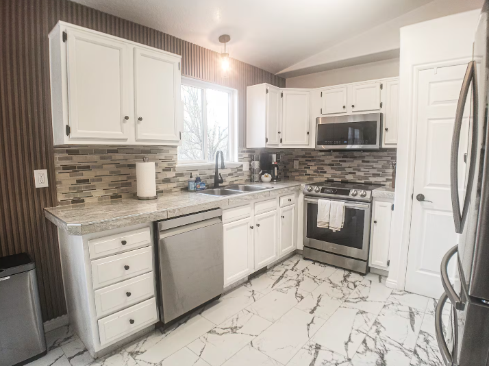 Remodeled kitchen with white cabinets, mosaic tile backsplash, stainless steel appliances and marble tile floors