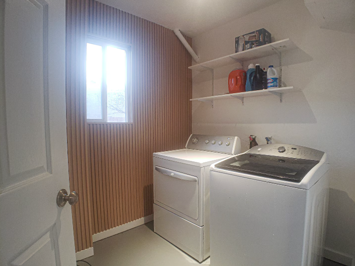In-unit laundry room with full-size washer and dryer, wood slat accent wall, shelving and natural light