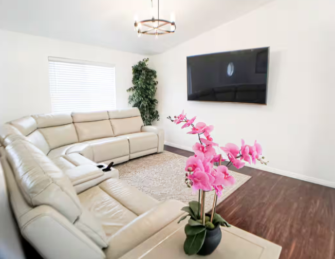 Bright living room with cream leather reclining sectional, large wall-mounted TV, chandelier and pink orchids