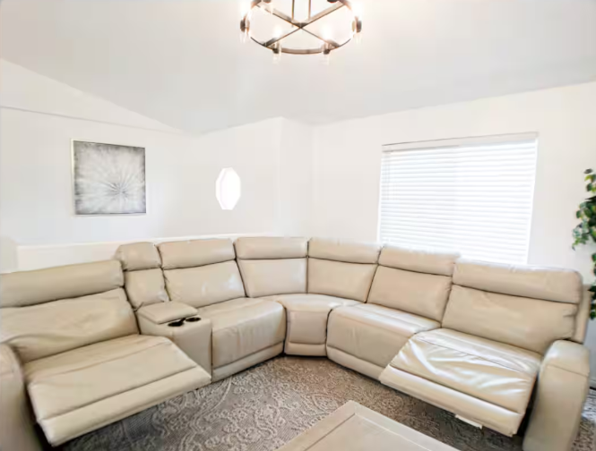Spacious living room with cream leather reclining sectional, chandelier, abstract artwork and large windows
