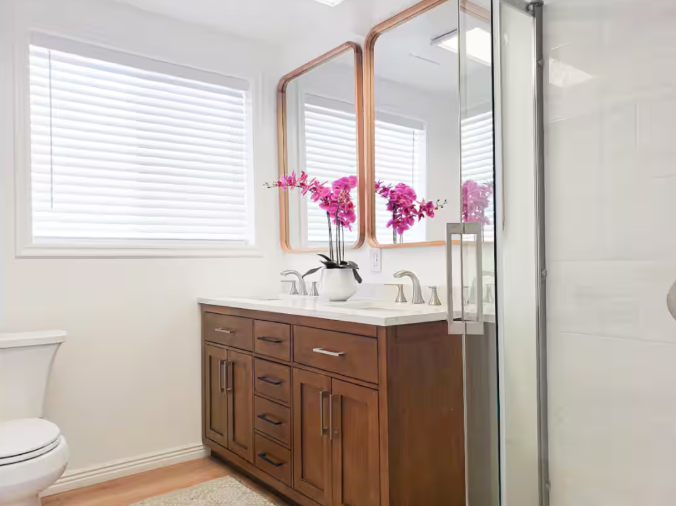 Remodeled bathroom with dual wood vanity, copper-framed mirrors, pink orchids and glass shower enclosure