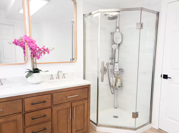 Bright bathroom with wood vanity, copper-framed mirror, pink orchids and corner glass shower