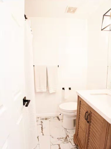 Clean white bathroom with marble tile floor, wood vanity and black fixtures