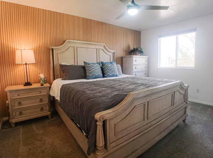 Master king bedroom with ornate wood furniture, orange striped accent wall and ceiling fan