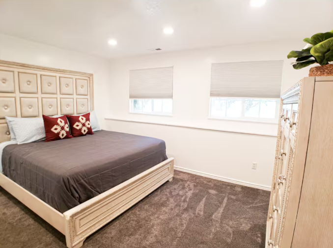 Bright queen bedroom with tufted upholstered headboard, red accent pillows and large windows