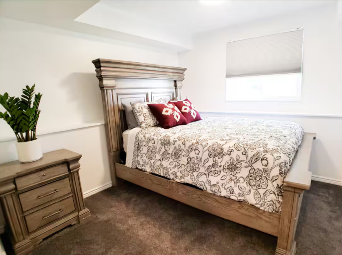 Cozy queen bedroom with ornate wood headboard, floral bedding, red accent pillows and potted plant