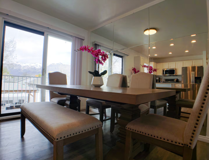 Bright dining room with farmhouse table, upholstered chairs, bench seating, pink orchids and mountain views through sliding glass door