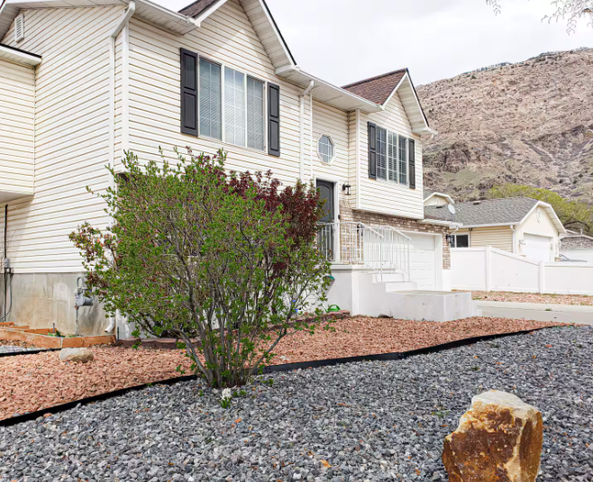 Two-story white home with black shutters, stone accents and Wasatch Mountain backdrop in spring
