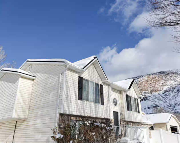 Two-story white home with snow-covered roof and dramatic Wasatch Mountain backdrop in winter
