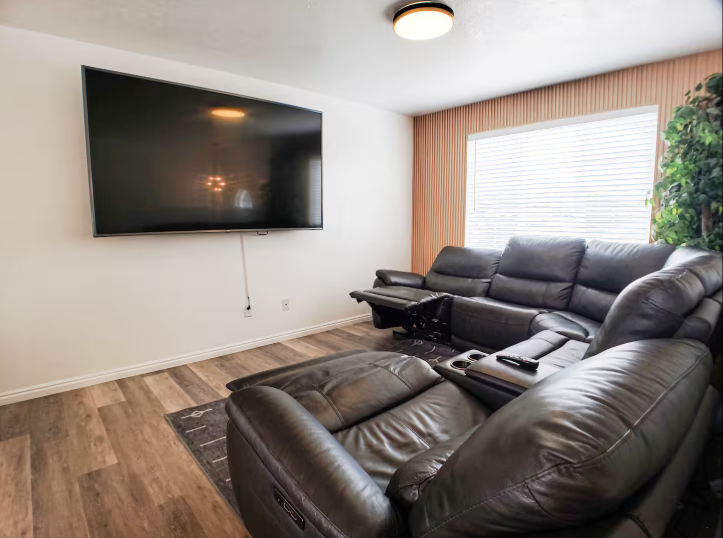 Media room with large wall-mounted TV, leather reclining sectional and wood accent wall