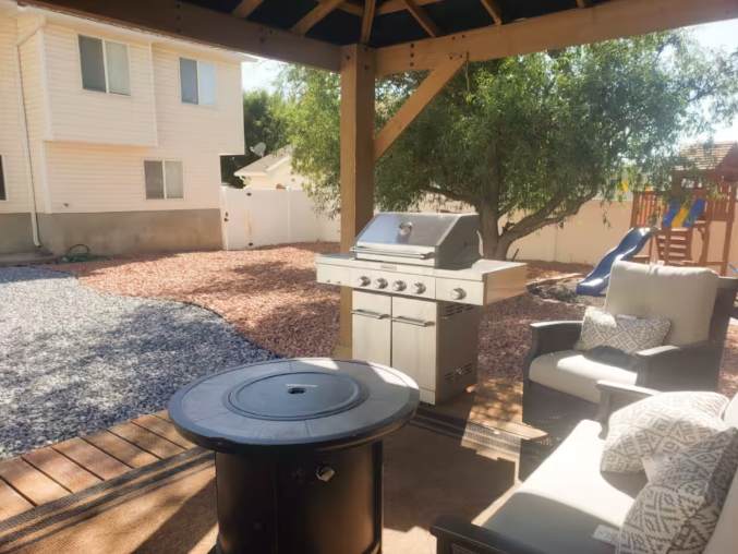 Covered patio with stainless steel BBQ grill, fire pit table and outdoor seating in fenced backyard