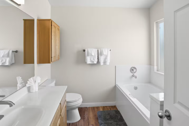 Bathroom with wood upper cabinet, gray shower curtain, white vanity with chrome faucet and fresh towels