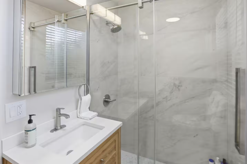 Modern bathroom with wood grain vanity, white quartz countertop, chrome faucet, medicine cabinet mirror and marble tile walk-in shower