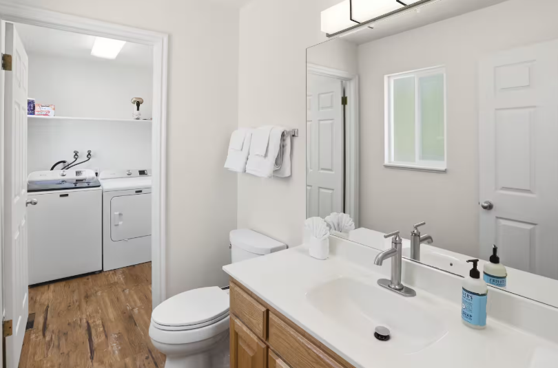 Bathroom with wood vanity, white countertop and open doorway showing washer and dryer in adjacent laundry room