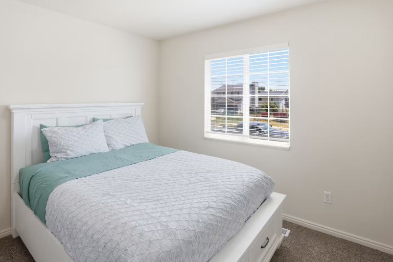 Queen bedroom with white panel headboard, teal and gray bedding, storage bed frame and bright window with plantation shutters