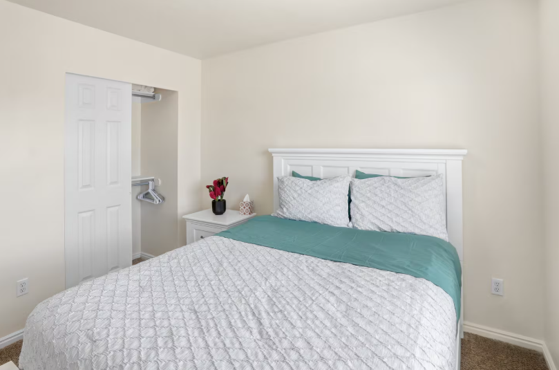 Queen bedroom with white panel headboard, teal accent bedding, walk-in closet and nightstand with flowers