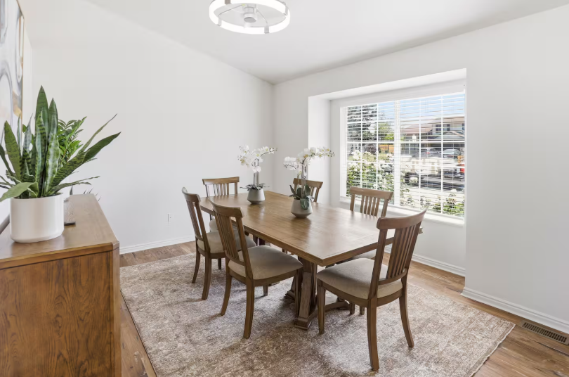 Bright dining room with wood trestle table seating 6, slat-back chairs, white orchids and large window with natural light