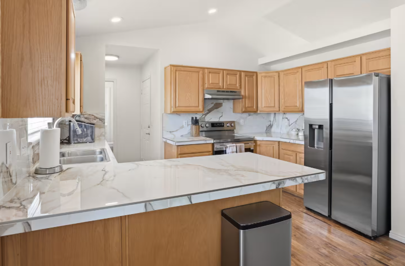Kitchen with honey oak cabinets, marble countertops, kitchen island, stainless steel appliances and hardwood floors