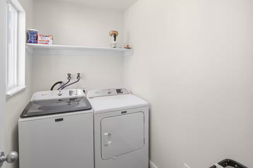 Laundry room with Maytag top-load washer and dryer, white shelf with supplies and bright window