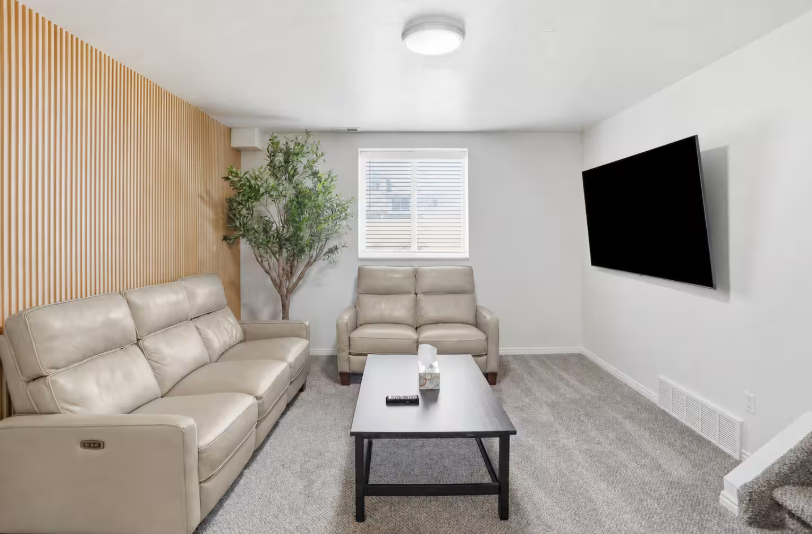 Lower level living room with cream leather power recliners, loveseat, wood slat accent wall, faux olive tree and large wall-mounted TV