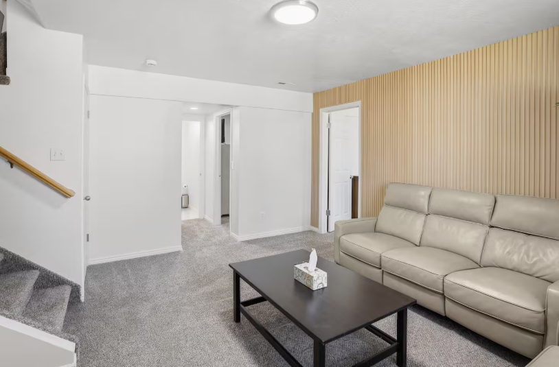 Lower level bonus room with cream leather sofa, wood slat accent wall, dark coffee table and staircase access