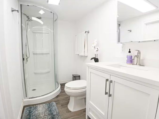 Bright white bathroom with curved glass shower, white vanity, and wood-look floors