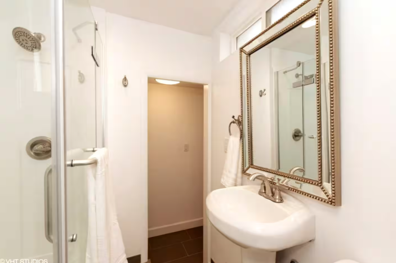 Bathroom with pedestal sink, framed mirror, and glass shower enclosure