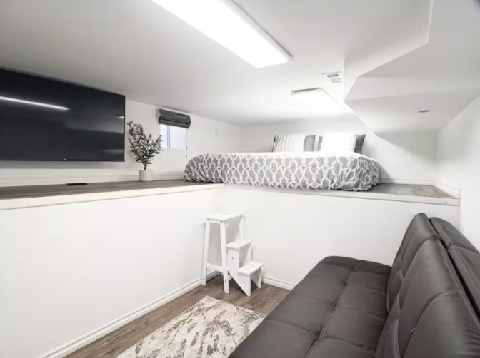 Loft sleeping area with two beds, wall-mounted TV, and leather sofa below