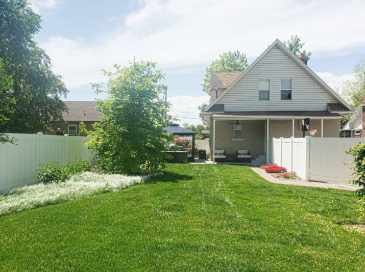 Spacious backyard with lush green lawn, mature trees, and covered back porch
