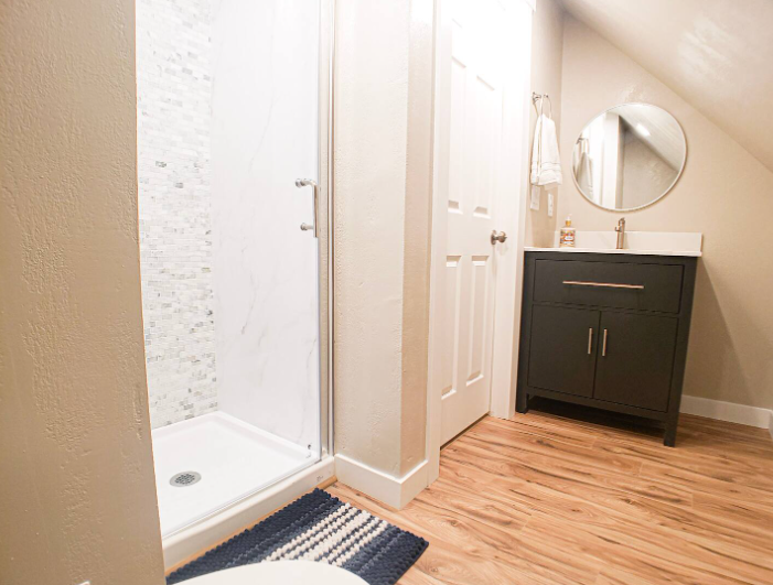 Attic bathroom with black vanity, round mirror, and marble-tile walk-in shower